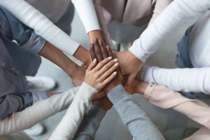 Top view of a diverse business team showing unity by placing their hands together in the center, symbolizing teamwork and collaboration. The hands are stacked neatly, with some palms facing down and others up, representing mutual support and collective effort.