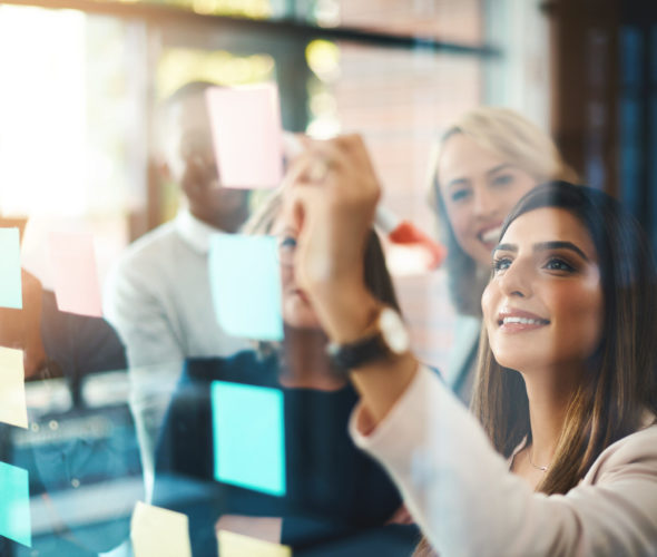 Shot of a group of businesspeople arranging sticky notes on a glass wall in a modern office